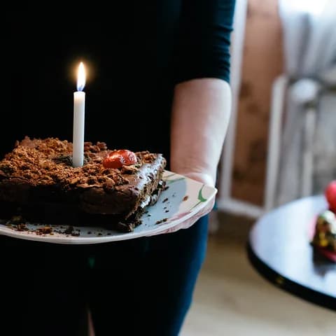 A hand holding a birthday cake with a lit candle