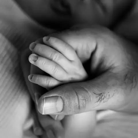 A parent's hand holding a newborn's hand